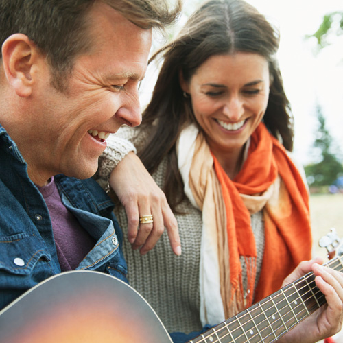 Ein Mann spielt einer Frau auf der Gitarre vor. Beide lachen