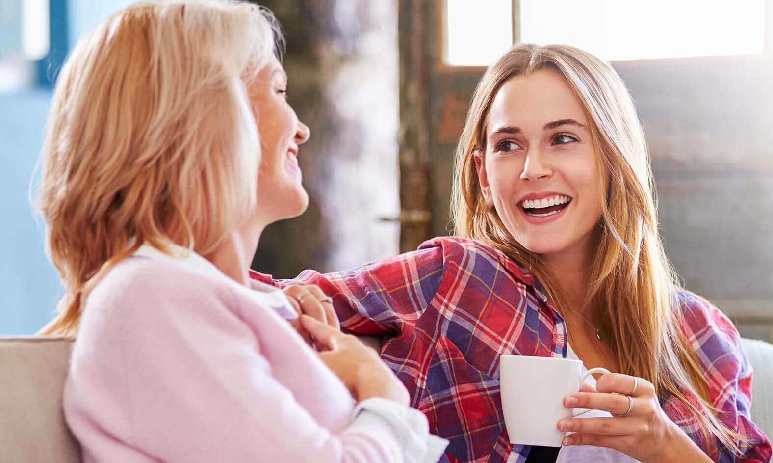 Zwei lächelnde Frauen unterhalten sich auf einem Sofa
