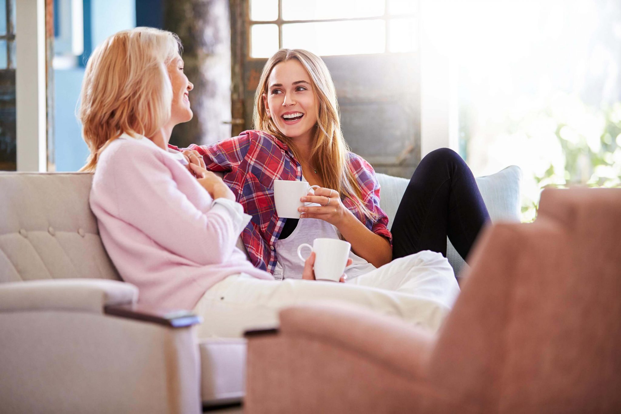 Zwei lachende Frauen unterhalten sich auf einem Sofa